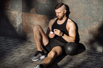 Fitness muscular man with weight ball resting and sitting against the concrete wall