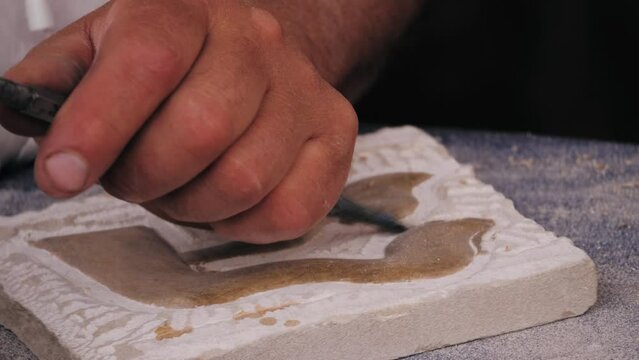 Craftsman making stone fresco close-up. Man hammering architectural relief. 