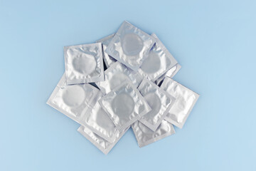 A lot of condoms in foil packaging lie on a blue background, in the center of the frame. Safe sex and reproductive health concept.