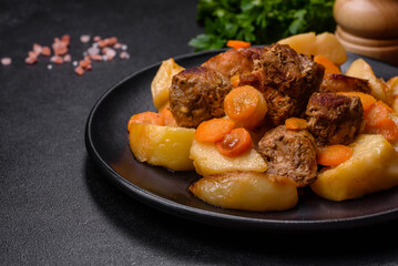Beef meat and vegetables stew on a black plate with roasted potatoes