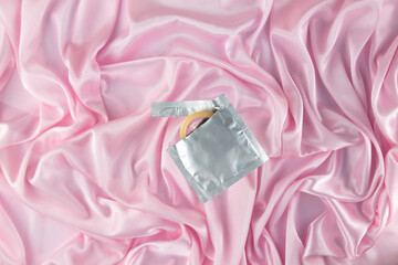 A piece of a condom sticks out of a foil package against a pink silk sheet. Safe sex and...