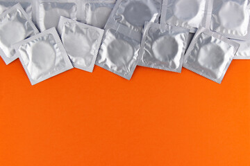 A lot of condoms in foil packaging lie on an orange background, at the top of the frame.  Lots of empty space