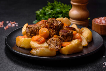 Beef meat and vegetables stew on a black plate with roasted potatoes