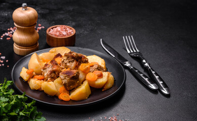 Beef meat and vegetables stew on a black plate with roasted potatoes