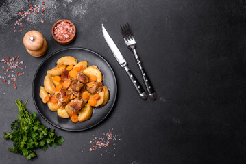 Beef meat and vegetables stew on a black plate with roasted potatoes