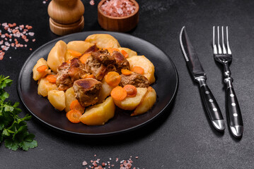 Beef meat and vegetables stew on a black plate with roasted potatoes
