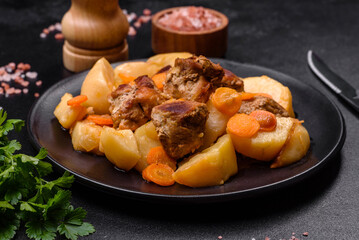 Beef meat and vegetables stew on a black plate with roasted potatoes
