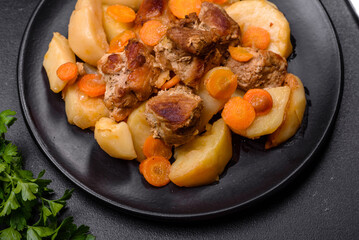 Beef meat and vegetables stew on a black plate with roasted potatoes