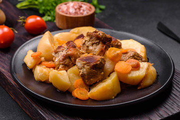 Beef meat and vegetables stew on a black plate with roasted potatoes
