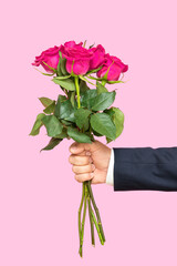 A man's hand holds out a bouquet of red roses on a pink background