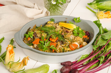 Oven baked vegetables with herbs in a baking dish on a white wooden background