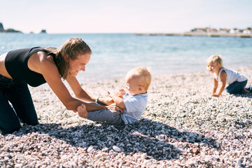 Mom tickles a little boy on a pebble beach. High quality photo - obrazy, fototapety, plakaty