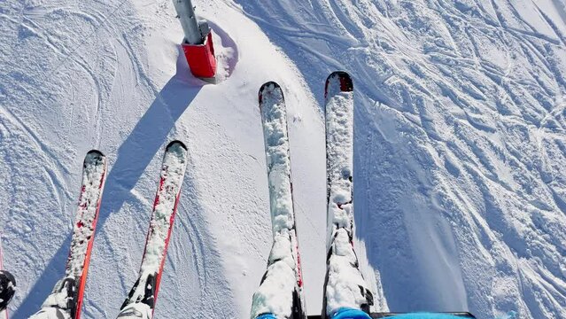 View from ski lift: legs and pairs of skis over skier below
