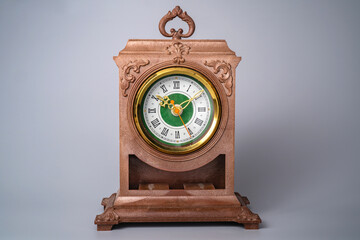 Old plastic table clock with gold stopped hands. Brown vintage watch with round white green dial and Roman numbers on isolated grey background. Front view of face aged clock. Retro timepiece.