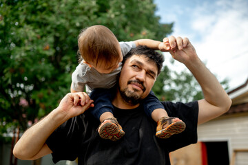 A little kid sits on dad's shoulders. They have fun, the father spends time with his son. The concept of a happy family