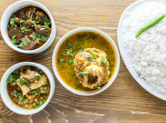 chicken korma, dal chana, kala bhuna gosht, chicken curry, plain rice with onion, pepper and salad served in a dish isolated on wooden table top view of indian and bangladesh food