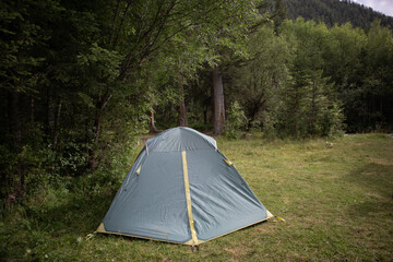 Camping in a tourist forest. A green tent set up on a picnic spot.