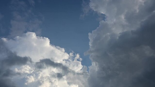 Time lapse of white puffy cloud becoming hidden by large blue-grey cloud.
