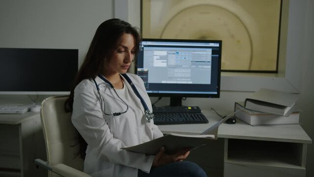 A young female doctor in a white coat is sitting at a table and studying a patient's medical history. X-ray technician