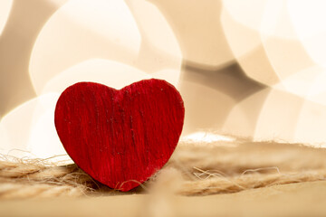 Valentine's Day greetings concept. Little red wooden heart close up, party lights bokeh on...