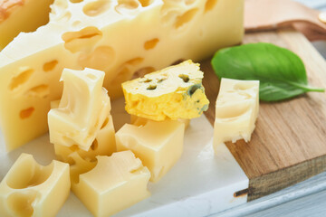 Piece of maasdam cheese and camembert, smoked cheese, blue cheese, parmesan, brie cheese with basil and pepper on white marble board white wooden old background. Set or assortment cheeses. Top view.