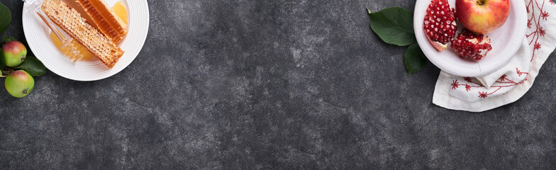 Rosh Hashanah. Honey jar, honeycomb, apple and pomegranate on dark grey old rustic concrete background table. Jewish New Year holiday greeting card. Rosh Hashanah holiday attributes. Banner.Top view.