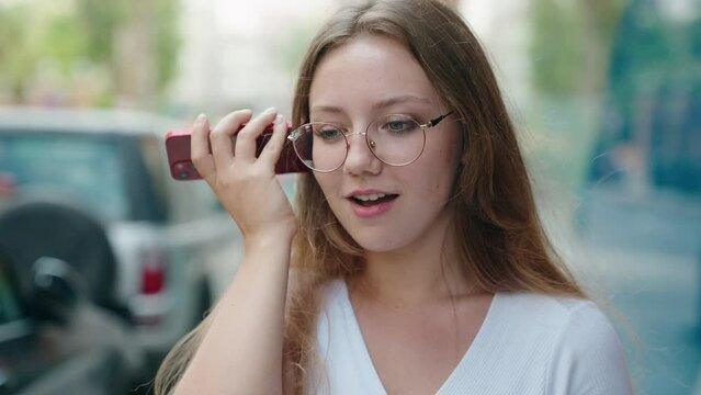 Young blonde woman smiling confident listening audio message by the smartphone at street
