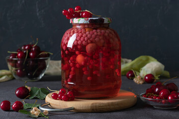 Homemade canned compote with sweet cherries and red currants in glass jar on dark gray background
