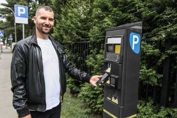 happy man pays for his parking space at the parking meter