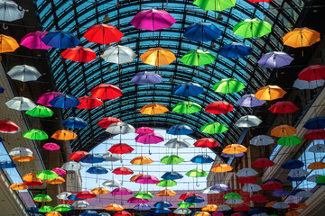 Lots of colorful umbrellas hanging high from the ceiling in a large room.
