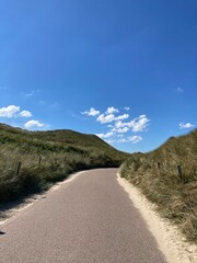A grass bordered path through dunes to the beach under blue sky