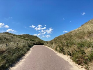 A grass bordered path through dunes to the beach under blue sky