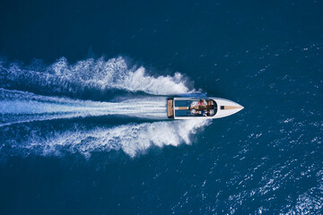 White speedboat fast movement on blue water top view. White large open boat with people moving fast...