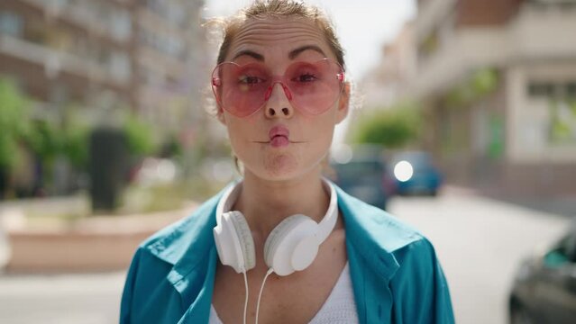 Young woman wearing heart sunglasses and headphones doing funny gesture with mouth at street