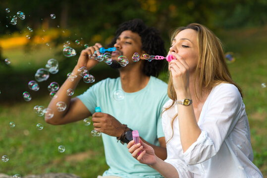 Mixed race couple blowing soap bubbles in the summer nature