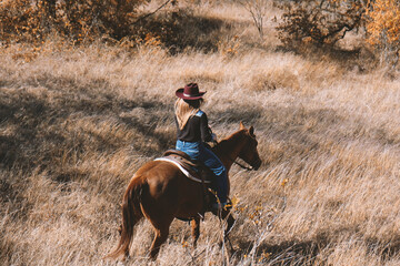 Cowgirl horseback ride down hill on horse through Texas autumn field during fall season.