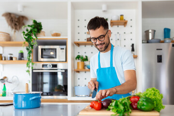 Handsome young man man stand at modern kitchen chop vegetables prepare fresh vegetable salad for dinner or lunch, young male cooking at home make breakfast follow healthy diet, vegetarian concept