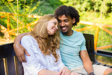 Young mixed race couple talking while sitting on the bench in the summer nature