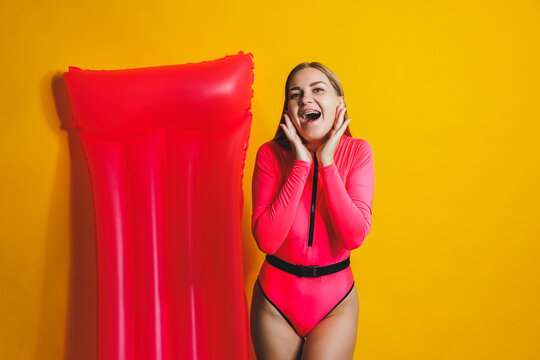 Beautiful young smiling woman wearing a pink swimsuit and posing on a yellow background with an air mattress, isolated on a bright yellow background
