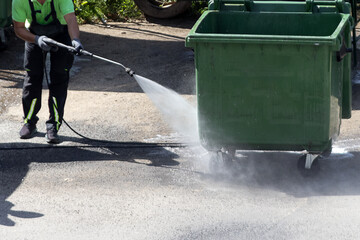 A municipal service worker treats a garbage container with a disinfectant solution. Washing the...
