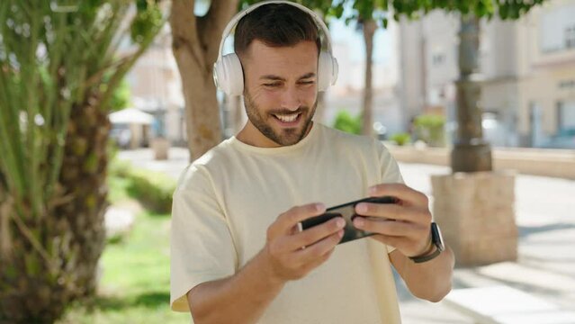 Young hispanic man smiling confident playing video game at park