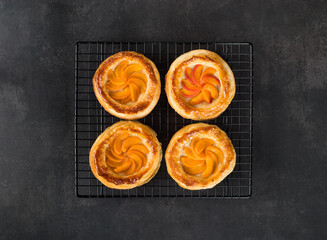 Small open pies made of puff pastry without yeast, with slices of apricots, on a serving metal stand. Dark grey background. Top view