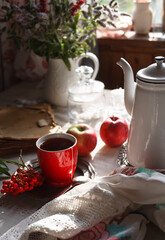 A cup of tea with a bunch of red rowan on metal plate, autumn morning tea concept.