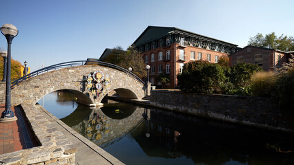 Day time autumn view of bridge in popular city park, Carroll Creek Park in historic district of Frederick Maryland with shops and building on sides of the canal. People walking.