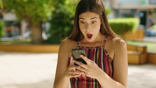 Young beautiful hispanic woman using smartphone with winner expression at park