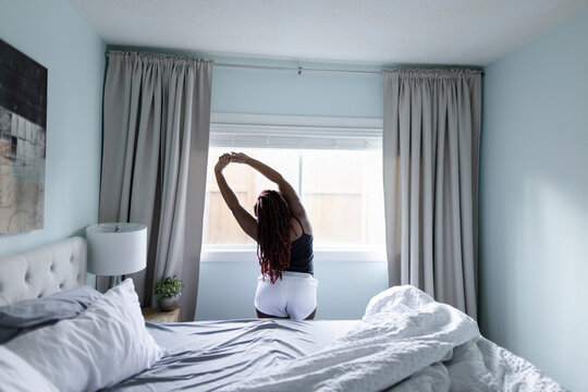 Woman in underwear stretching arms overhead at bedroom window