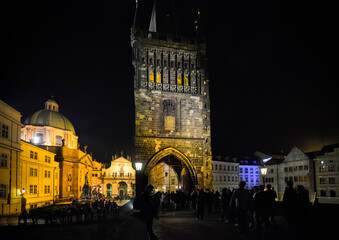Tourists and local Czech enjoy a late night on the Charles Bridge as they cross under the gothic Old Town Bridge Tower, in Prague, Czech Republic