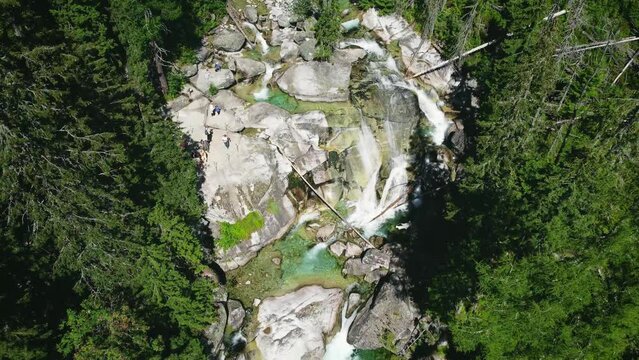 Aerial footage by drone (top view) of Waterfalls in High Tatras - Slovakia with crowd of tourists watching a wild forest river (stream). Summer season in mountains - crystal clear water of waterfall.
