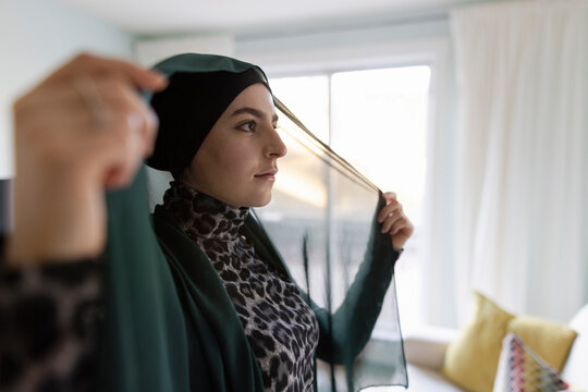 Beautiful young woman putting on hijab at home