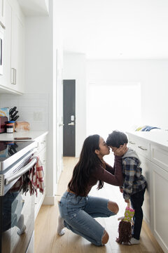 Affectionate mother kissing cute son on forehead in kitchen